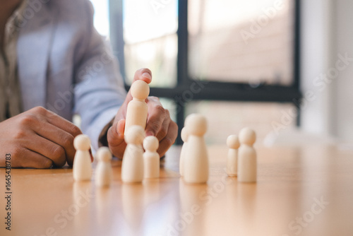 Leadership and teamwork concept with a business person arranging wooden human figures on a table, representing organizational management, strategy and human resource planning in the workplace.