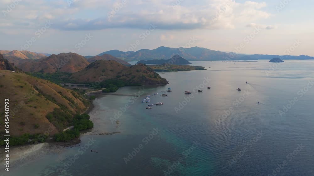 Aerial panorama of multiple boats anchored near green mangrove coastline and rolling hills in Komodo Aerial panorama of multiple boats anchored near green mangrove coastline and rolling hills in Komodo