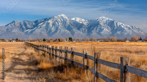 Rustic wooden fence lines a field stretching to snow-capped mountains.