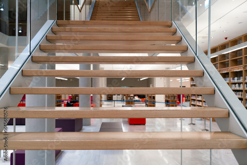 The clean and simple design of a modern flight of stairs made of light wood and glass. This interior shot from a library is perfect for architecture, design, and educational background concepts.

