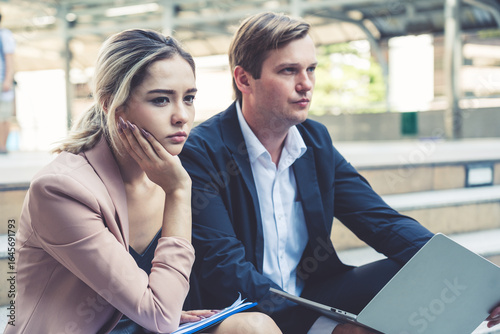 Bild auf Leinwand A male and female business colleague look concerned and thoughtful while working on their laptop in a city