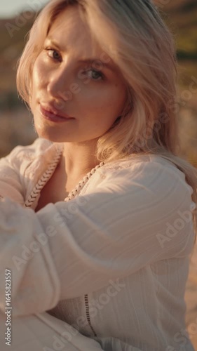 Confident young woman smiles slightly at the camera as the golden light of sunset glows on her face.