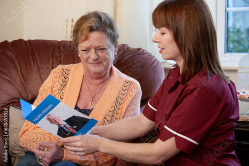 A care worker shows an elderly woman a health leaflet during a home visit as they discuss the information provided.