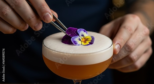 A bartender carefully places a vibrant flower garnish on a cocktail's foamy top.