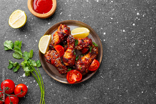 Spicy chicken wings with sriracha sauce and lime in a plate on dark background top view