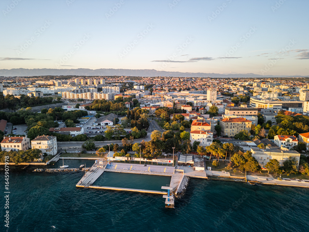 Obraz premium Aerial drone photo of Zadar Diving Board and Bazen Kolovare in Croatia, with the Adriatic Sea and expansive sunset sky creating a serene coastal scene during golden hour.