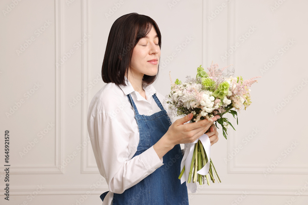Florist with beautiful bouquet of flowers near white wall indoors Florist with beautiful bouquet of flowers near white wall indoors