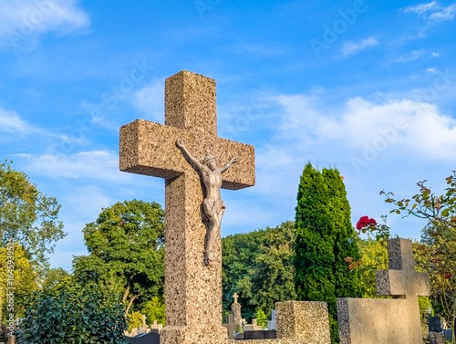 Fotografía Stone cross monument standing against clear blue sky with green foliage backgrou
