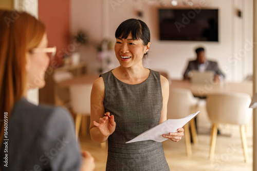 Fotografia Happy businesswoman discussing financial report with female coworker while stand