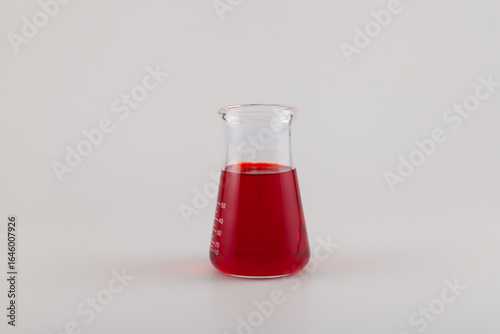 Red liquid in glass lab flask. Powder of Allura Red AC dissolved in water. Azo dye. Color index of 16035. Food additive E129. Colorant used in cosmetics, drugs, and food