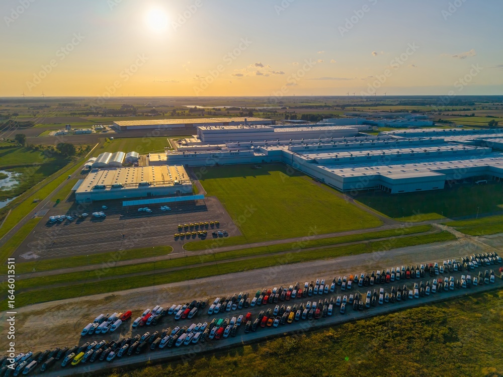 Fototapeta premium Aerial view of a car manufacturing plant at sunset, producing combustion and electric cars.