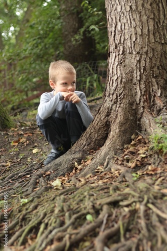 a child squats near a tree against the backdrop of beautiful roots protruding from the ground