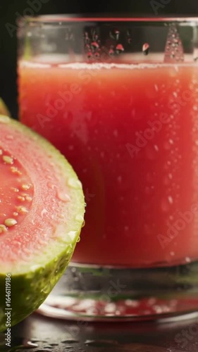 Close-up of a glass of fresh pink guava juice with halved tropical fruit, camera panning, condensation and water droplets