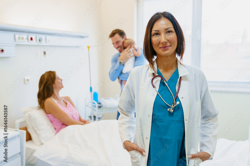 Obraz premium Confident Female Doctor in Scrubs with Patient Family in Bright Hospital Room