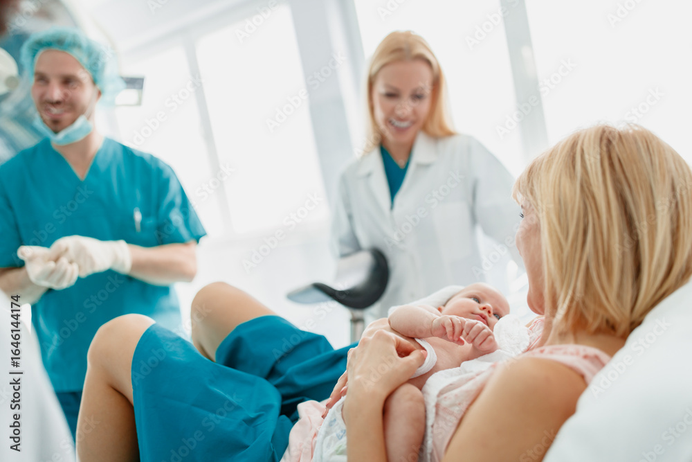 Obraz premium New Mother Holding Newborn with Supportive Medical Team in a Well-Lit Hospital Room