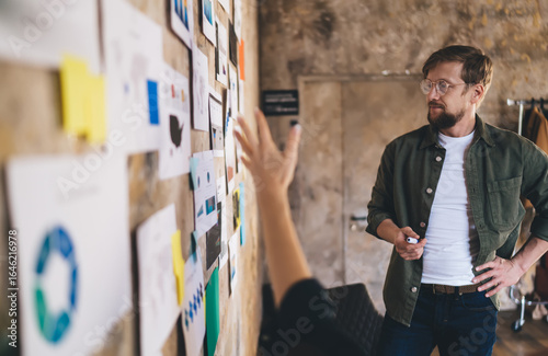 Принти на полотні Focused male entrepreneur listening to UX strategy pitch, analyzing complex data wall with user insights and tech diagrams during planning sprint in modern workspace