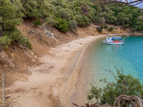 Fotografie a small white fishing boat floating in a secluded bay with clear blue-green water and a sandy beach, surrounded by a steep, wooded bank, travel and tourism
