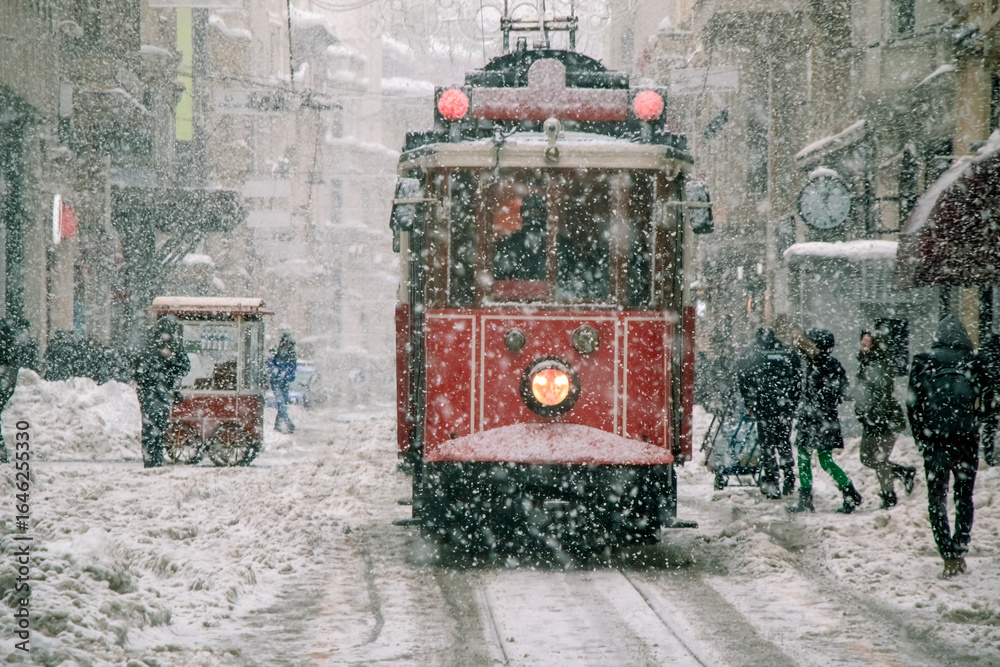 Fototapeta premium Istanbul’s iconic red tram glides through snowy Istiklal Street in Beyoglu, Turkey, offering a nostalgic winter scene in the city center.