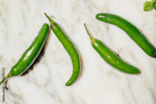 Fotografija four green serrano chili peppers on white marble