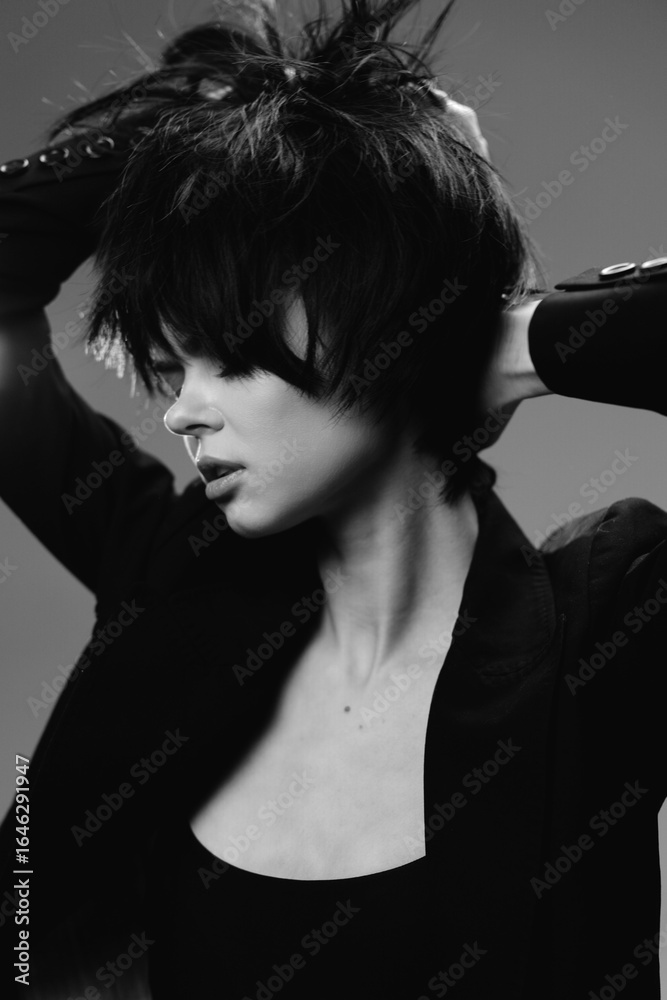 Naklejka premium Black and white portrait of a young woman with short hair posing with raised arms in stylish dark clothing