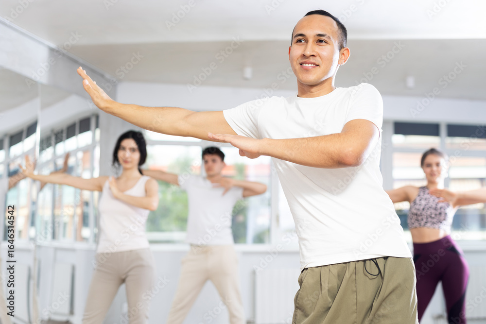 Fototapeta premium Guy conducts lesson for group of young people, demonstrates basic movements for performing locking dance, teaches modern dance culture directions