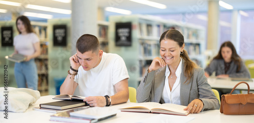 Young guy and young woman students reading book sitting at table in library