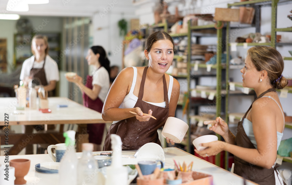 Obraz premium Positive young girls in apron processing clay bowls in carpenter's workshop