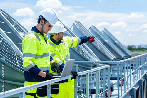 Industrial engineer teamwork working maintenance building exterior cooling systems. Male technician worker in safety uniform working and inspect pipeline valves air HVAC systems at construction site