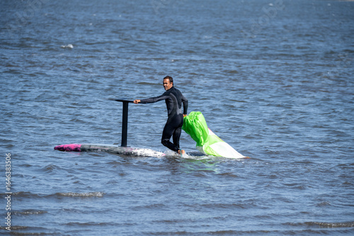 Valokuva A middle-aged man in a wetsuit on a hydrofoil board prepares to glide, with his