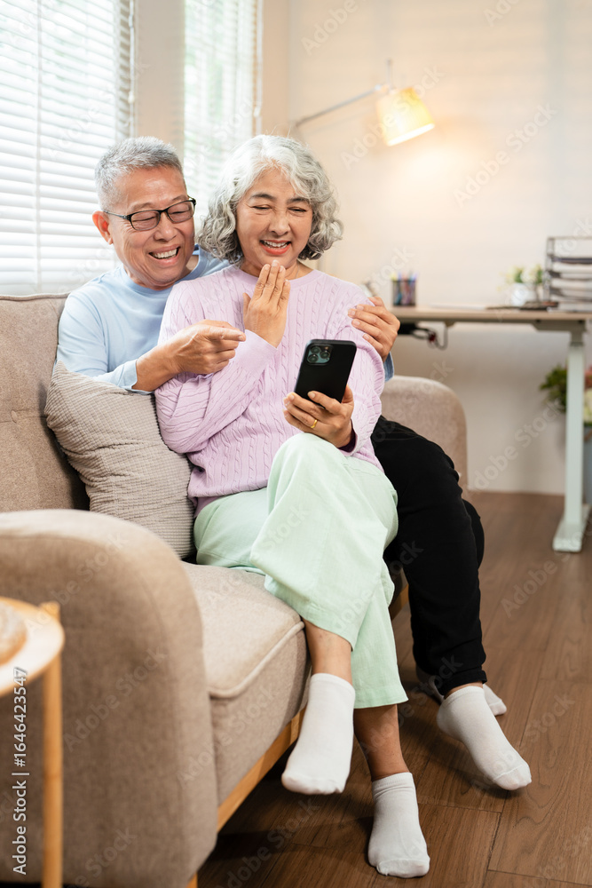 Happy 60s older couple holding mobile phone video conference calling by social distance virtual family online chat meeting sitting on couch at home. Happy 60s older couple holding mobile phone video conference calling by social distance virtual family online chat meeting sitting on couch at home.