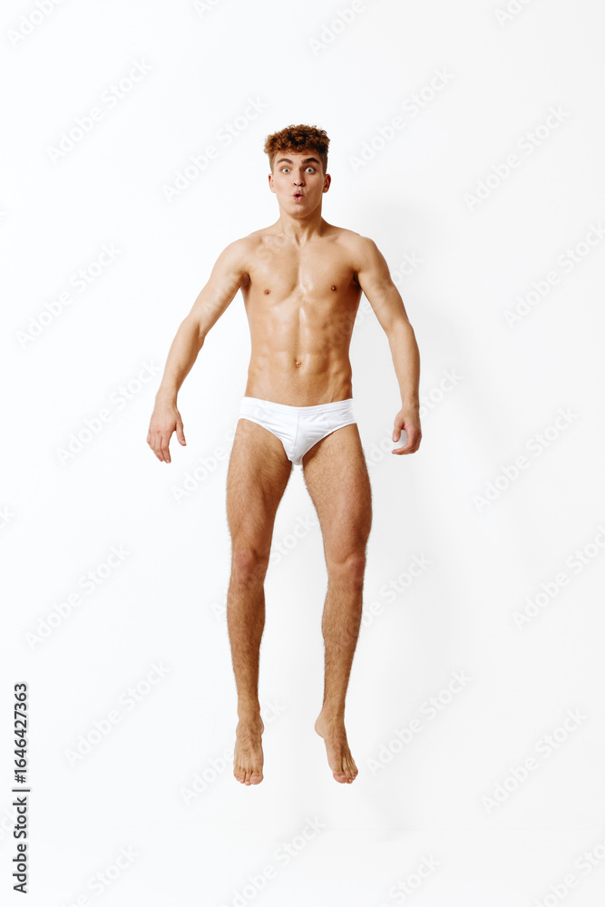 Fototapeta premium Athletic young man in white underwear jumping against a plain white background, showcasing energy and vitality. Dynamic movement and fitness concept.