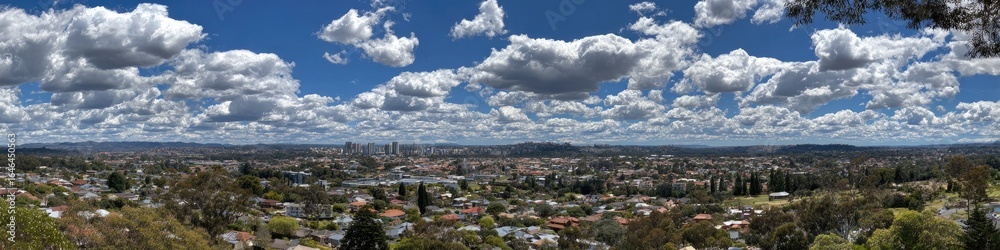 Fototapeta premium Panoramic view of a city nestled amongst hills, with a vibrant sky filled with fluffy clouds