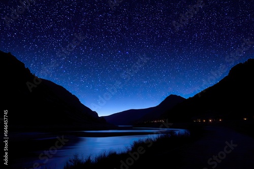 Night sky over a dark river valley. Silhouettes of mountains frame a tranquil river scene under a star-studded night sky