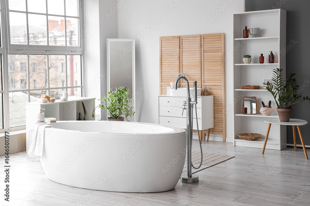 Fototapeta premium White bathtub in interior of spacious bathroom with panoramic windows