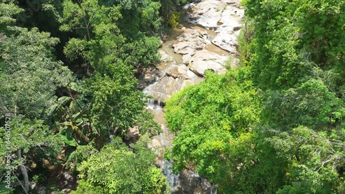 Aerial top-down view of a hidden creek in a dense jungle valley, Looking down on a rocky waterfall from the canopy, Unspoiled nature of a tropical rainforest stream