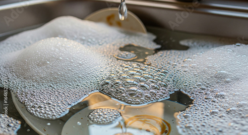 close-up of dishwater filled with bubbles and suds, reflecting a soft light source.