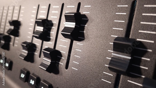 Close-up view of fader sliders and control buttons on a professional lighting control panel.