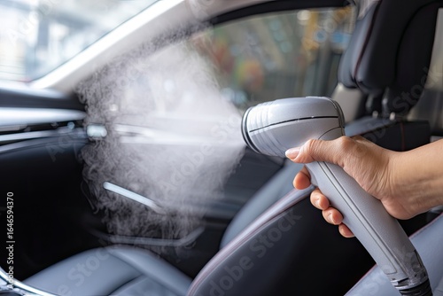 Steam cleaning car interior.  Hand holds a gray steamer, emitting steam to clean a dark car seat