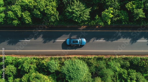 High-angle view of a light-blue car on a highway, surrounded by lush green trees