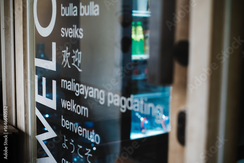 Multilingual welcome sign decal  on the transparent glass door of a tourist spot kiosk selling cold beverages with a refrigerator seen on the background
