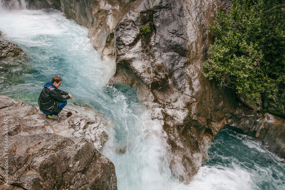 Fototapeta premium A man stands on the edge of a cliff above a waterfall in Sapadere Kanyonu, Sapadere, Antalya Province, Turkey