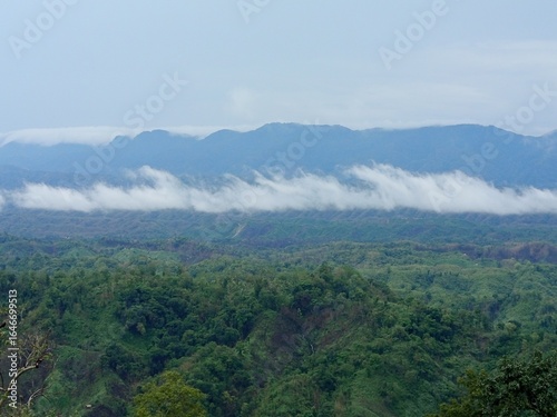 An expansive natural vista showcasing lush green mountain ranges partially veiled by atmospheric mist, creating a serene and captivating landscape.