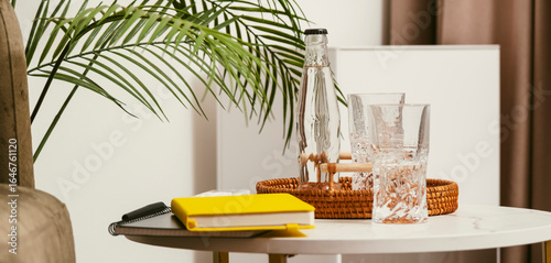 Fototapeta Naklejka Na Ścianę i Meble -  Refreshment station with water, glasses, and stationery on a table beside a plant in a modern living space