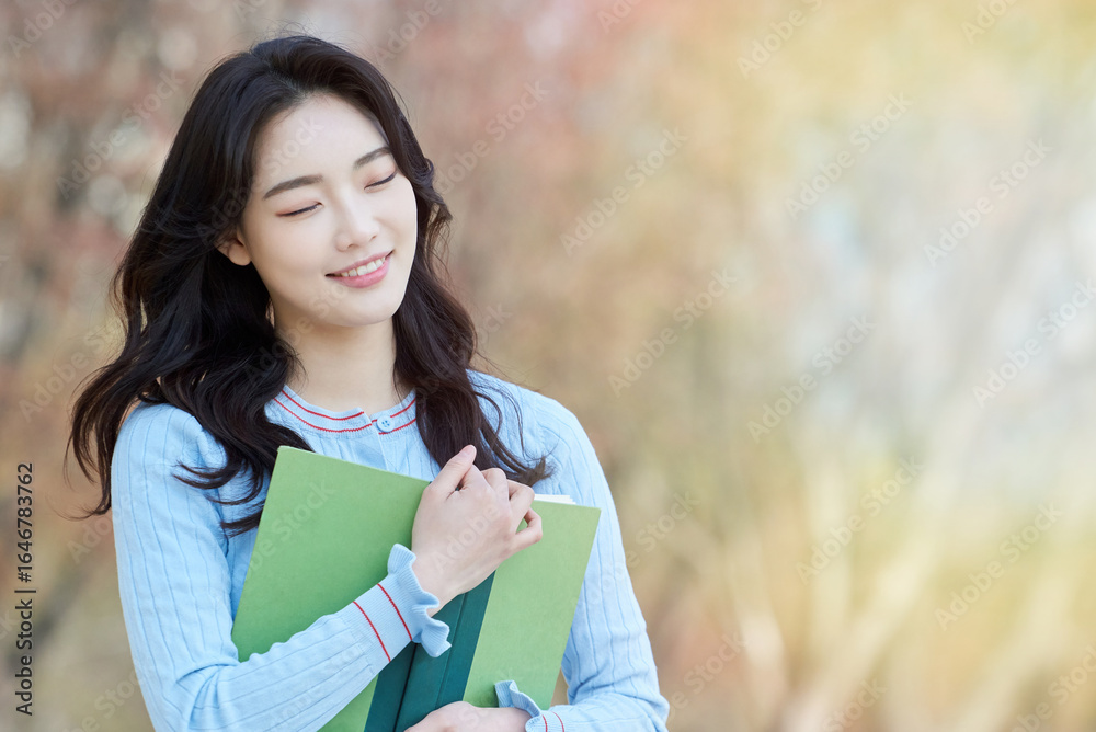 Young Asian female student holding books outdoors in springtime park
Young Asian female student holding books outdoors in springtime park
