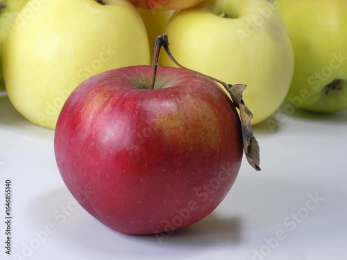 Red apple with a leaf on a background of yellow apples.