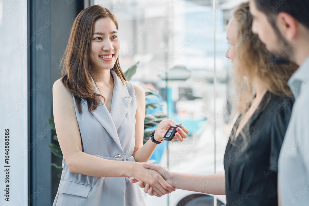 Obraz premium Professional female car dealer shaking hands and giving keys to smiling customer, symbolizing trust, joy, and success in automotive purchase and customer relations.