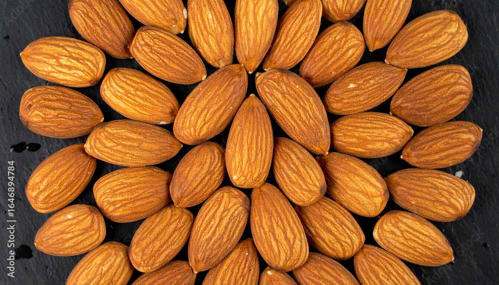 Fototapeta premium Almonds arranged in a circular pattern on a dark, textured surface.