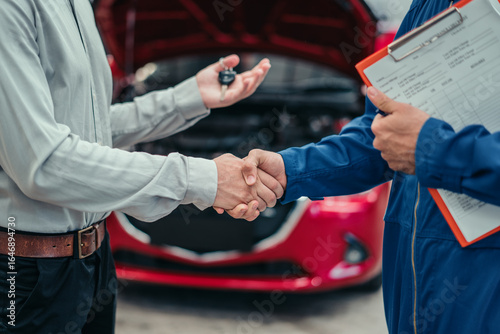 Satisfied car owner shaking hands with mechanic in blue uniform, showing trust, repair success, and satisfaction in automotive repair industry.