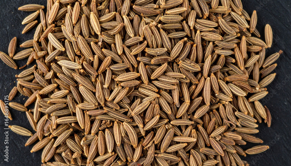 Close-up view of a pile of cumin seeds, showcasing their texture and color against a dark background. Close-up view of a pile of cumin seeds, showcasing their texture and color against a dark background.