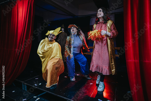 Photos The image depicts three actors enthusiastically performing in vibrant costumes on a theatrical stage surrounded by red curtains, showcasing an exciting and colorful performance